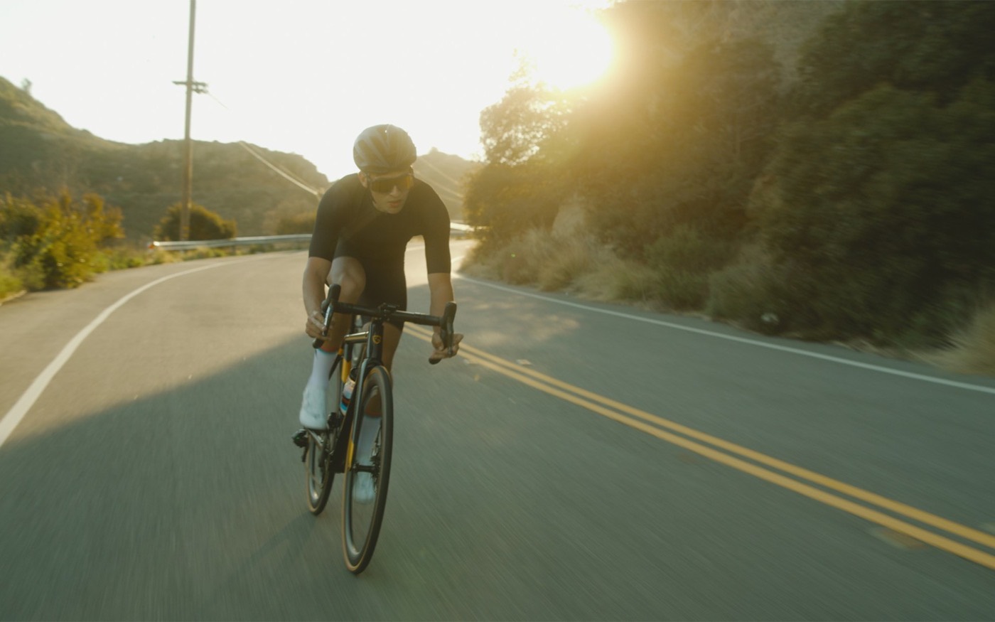 A cyclist riding a road bike into low golden light on an open road