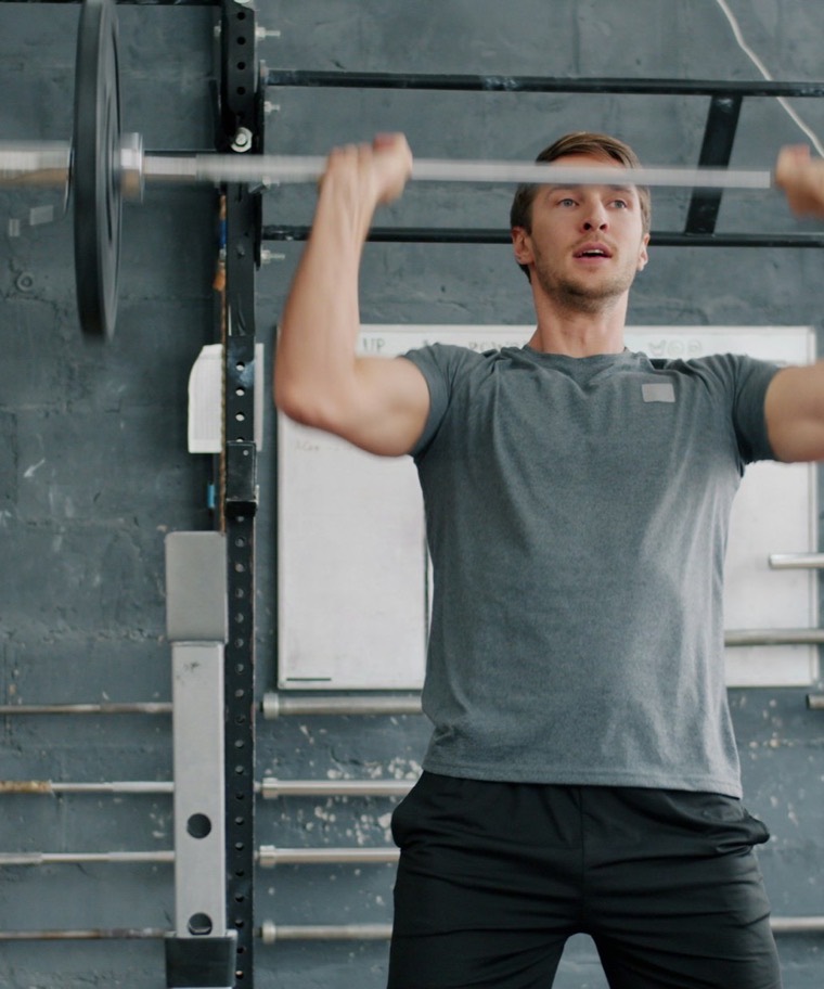 A man pressing a loaded barbell overhead in a gym