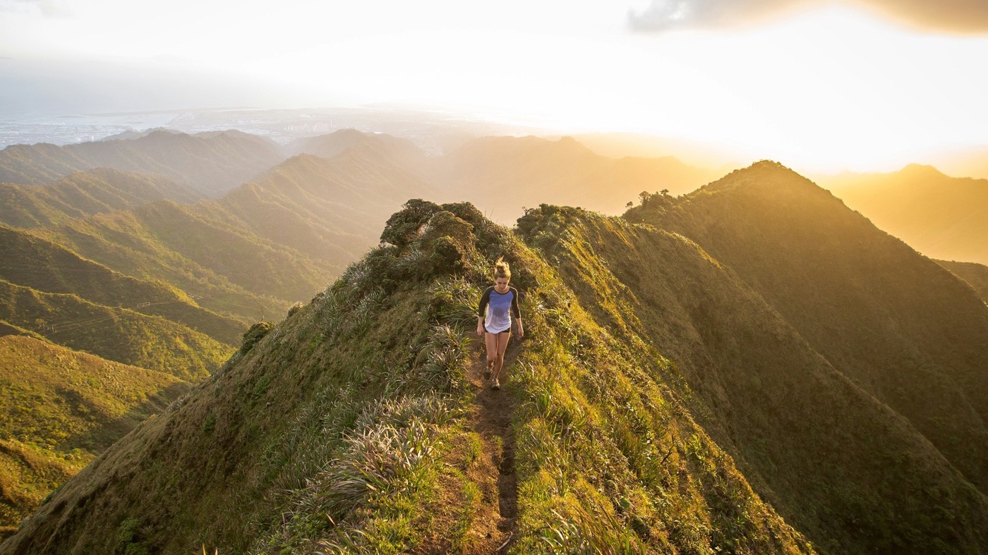 A person walking a narrow mountain ridge trail at golden hour