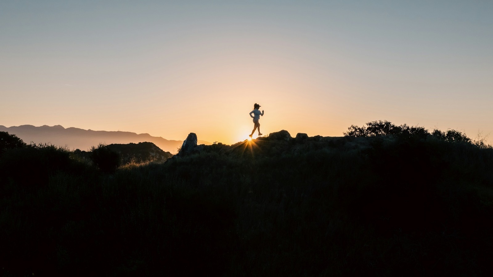 A runner silhouetted against the sun cresting a ridge at sunrise